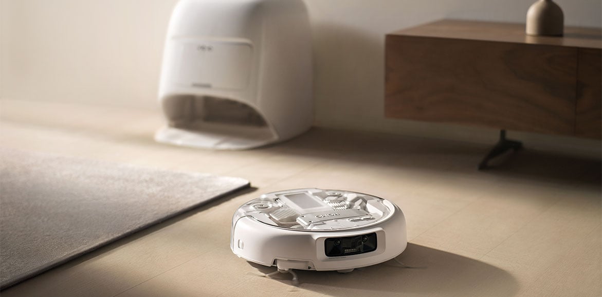 Robot sprzątający DJI ROMO A sprząta podłogę, za nim znajduje się stacja dokująca